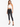 A model poses in a white crochet halter top and black skinny jeans, complemented by strappy black heels.