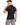 A man with short hair wearing a fitted black t-shirt, looking over his shoulder against a white background.