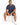 A man sits on a white cube wearing navy shorts and a matching t-shirt, paired with white sneakers.