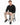 A man sits on a black stool, wearing a textured black sweatshirt, beige pants, and black sneakers.