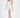 A model poses in a fitted white dress with a thigh-high slit, paired with nude heels and minimal accessories.