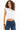 Model in Carbon Maya Padded Crop Top in white with elastic hem and blue jeans against a white background.